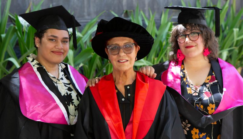 Two students and an academic wear academic dress, prepared for graduation.
