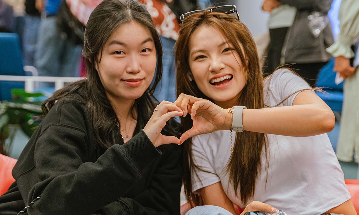 Two students making a heart shape with their hands