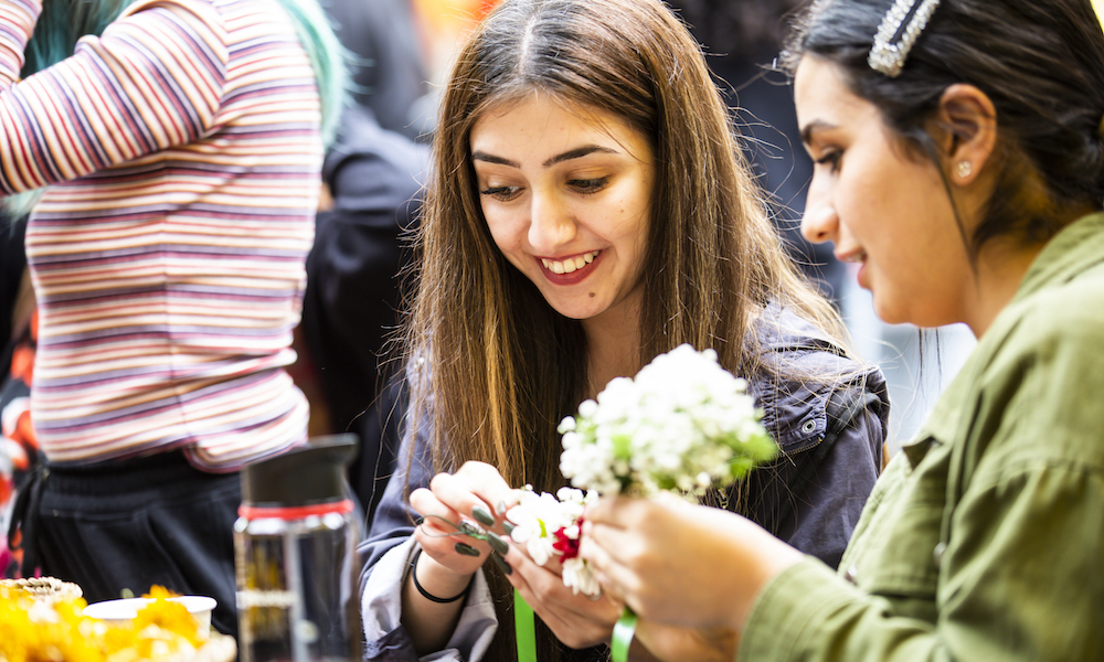 Two students smiling making flower crowns