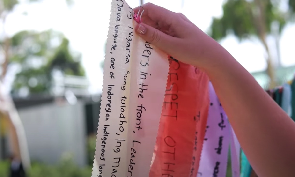 A hand hangs a message written on a ribbon onto a bunting.