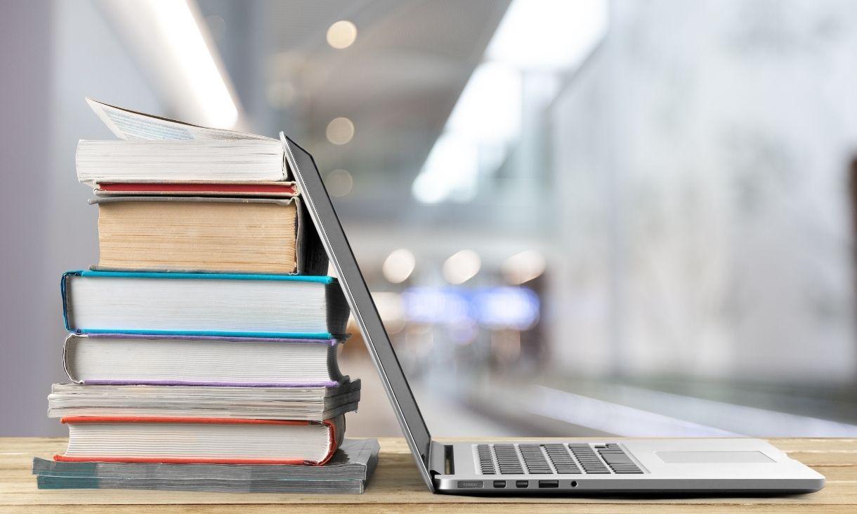 A laptop leaning against a stack of books.