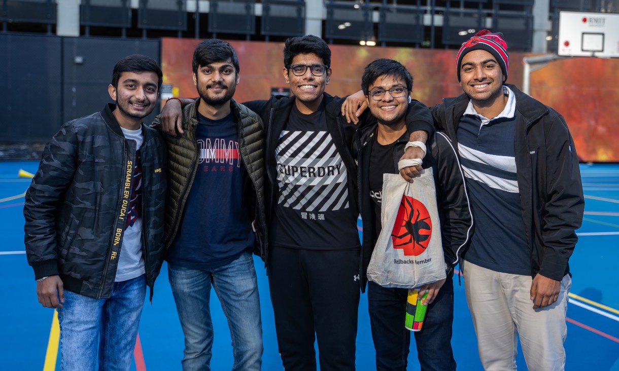 five students smiling toward camera, arms around each other