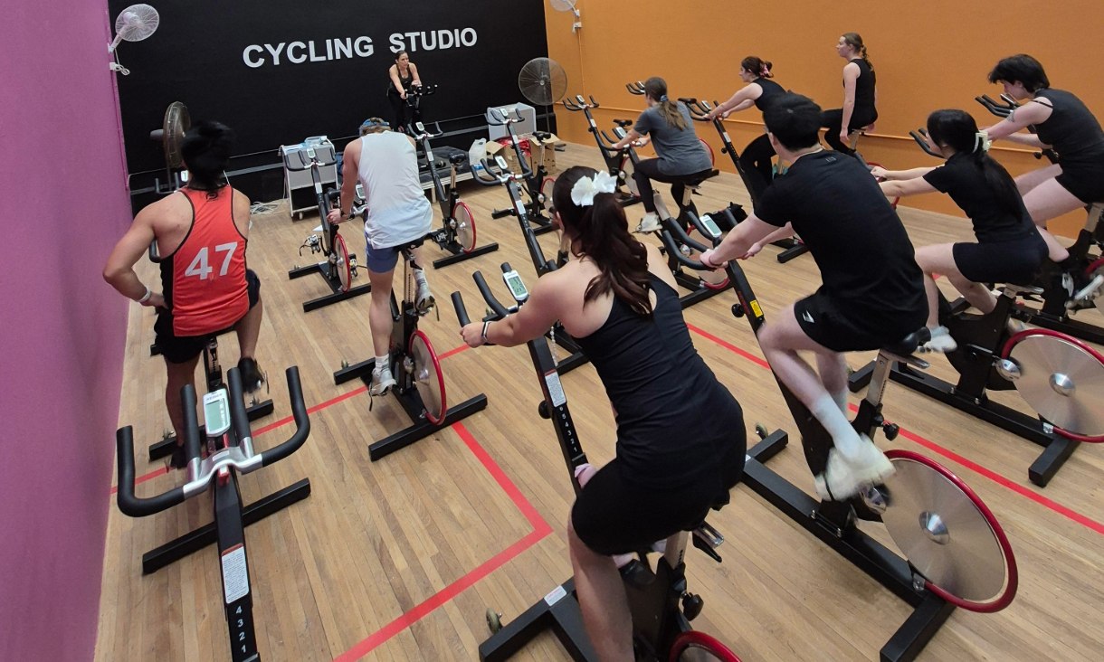 Participants taking part in an instructor-led spin class in the RMIT Sports Centre cycling studio, using stationary bikes arranged across the room.