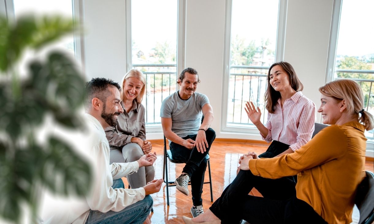 Group of people seated in a circle participating in discussion or support group.