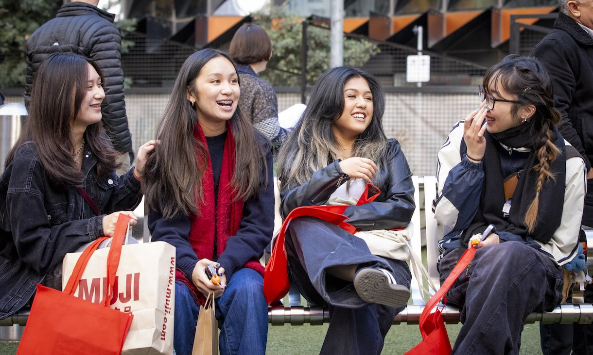 Four students sit on a bench laughing and smiling.