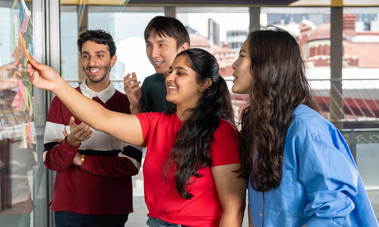Students collaborating with sticky notes on a glass wall during a group brainstorming session in a classroom.