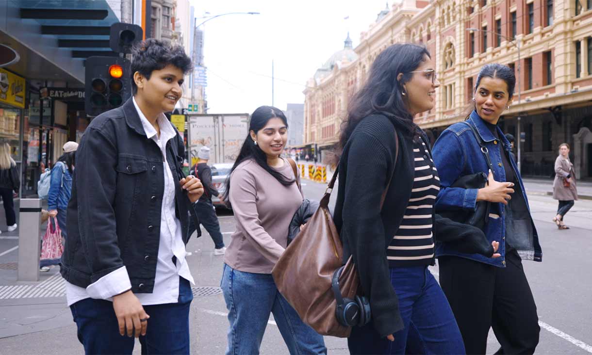 Group of students walking across a busy intersection outside Flinders Street Station in Melbourne, carrying bags and chatting.