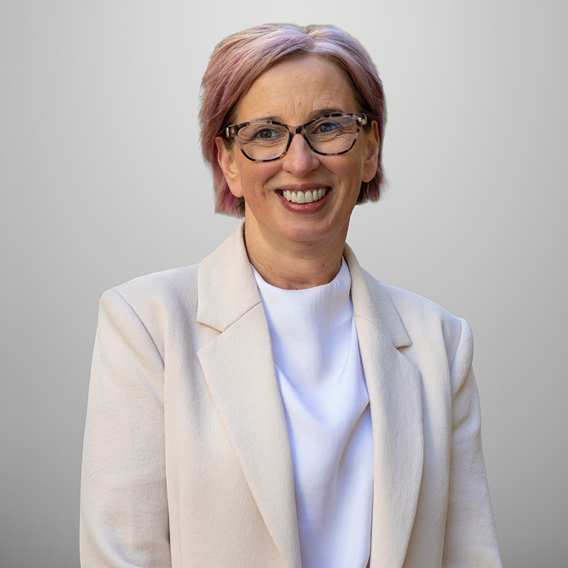 Women wearing a cream blazer and white top, standing against a plain grey background.