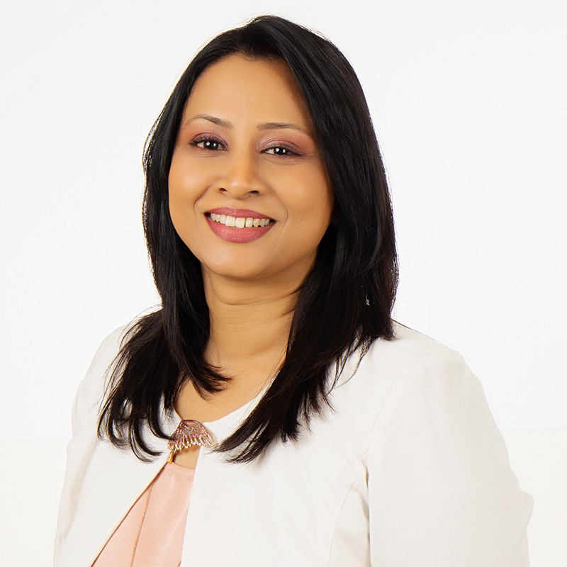 A women wearing a peach and white color shirt, looking towards the camera and smiling.