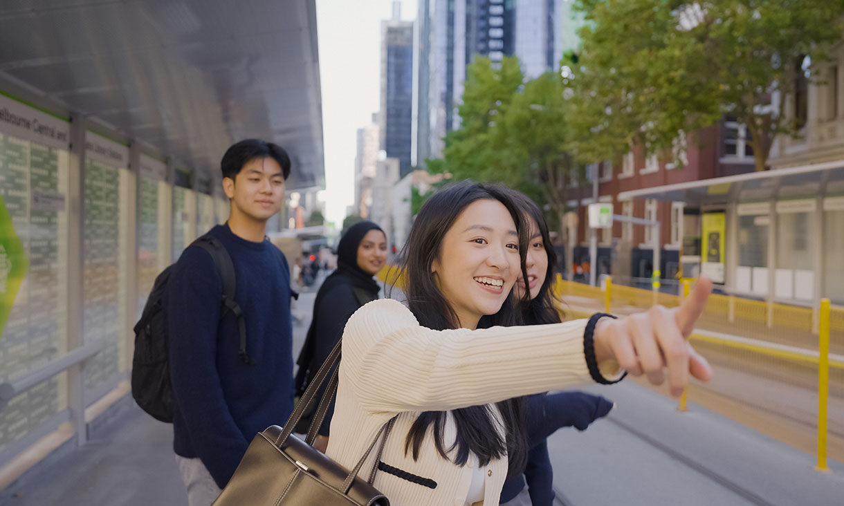 Student pointing while standing with friends at a city tram stop.