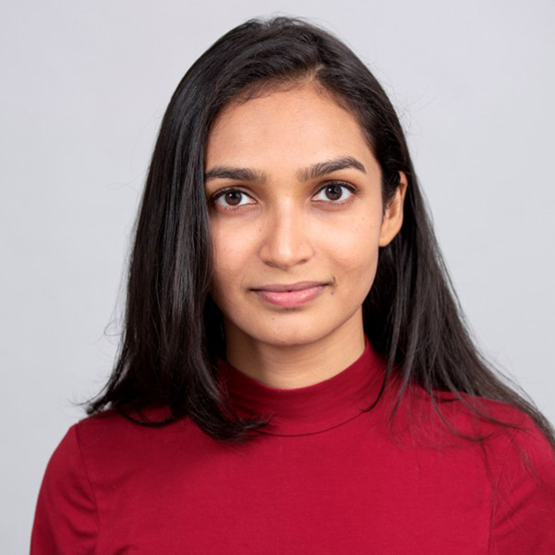 A women wearing a maroon color t-shirt, looking towards the camera and smiling. 