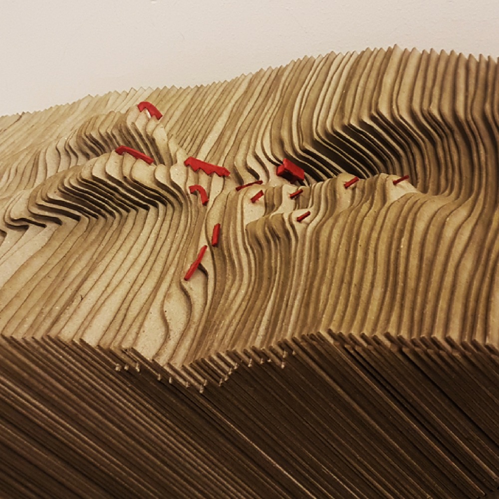 Layered cardboard topographic model with small red structures.