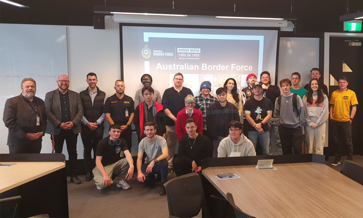 A group of students pose in front of a powerpoint presentation in a classroom.