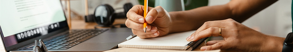 A person writes notes from their laptop onto a notepad.