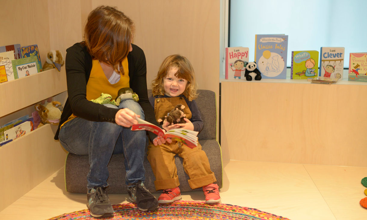 A childcare teacher reads a book to a toddler.