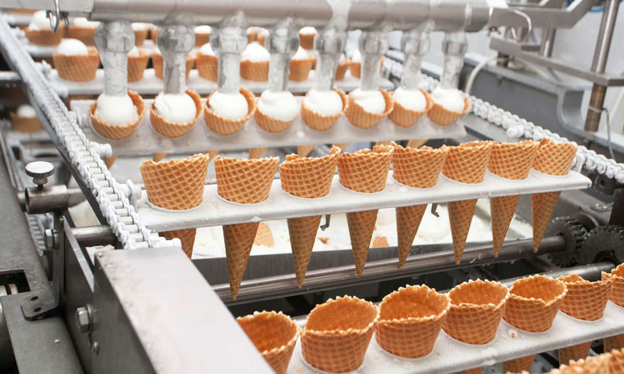 An ice-cream machine fills waffle cones with ice-cream.