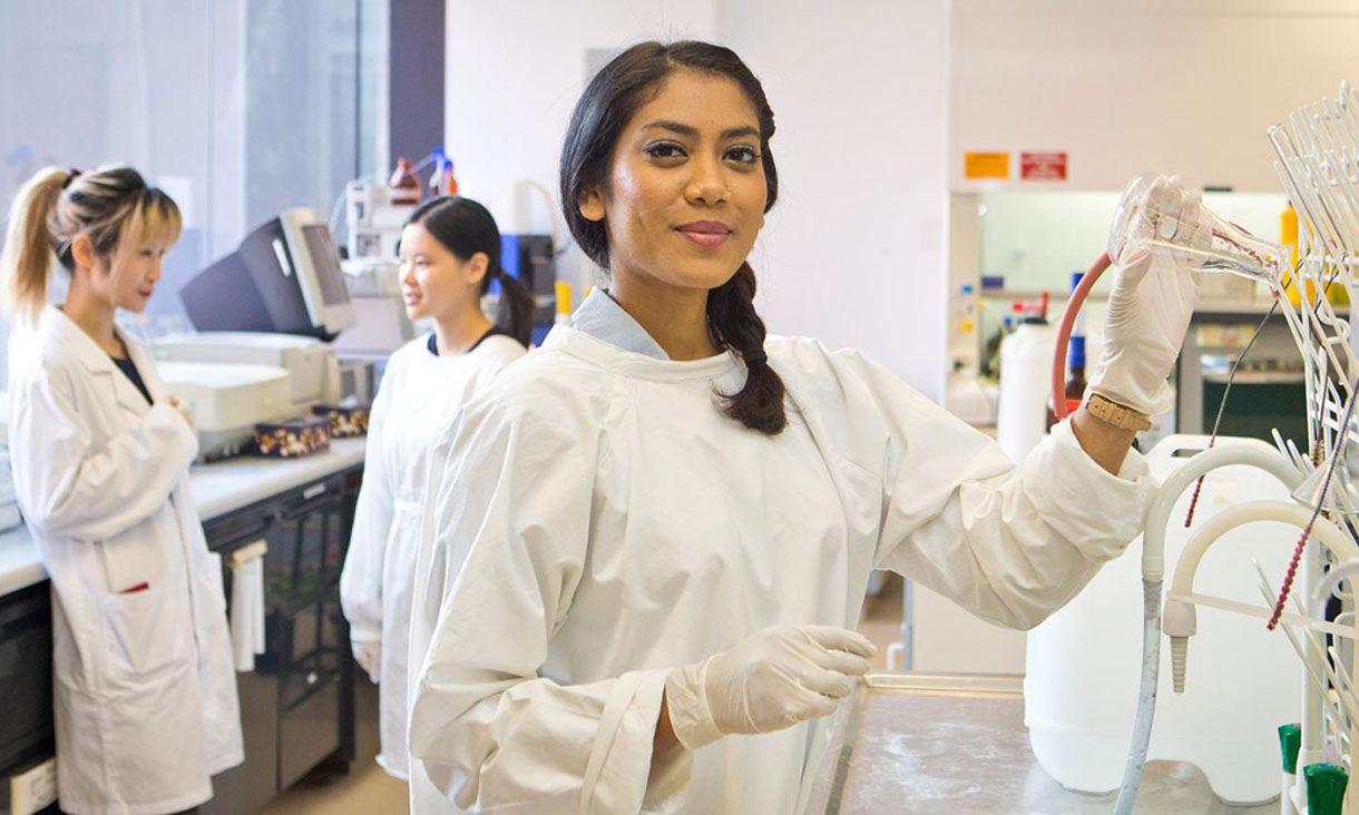 3 lab technicians in a lab. One poses for the camera.