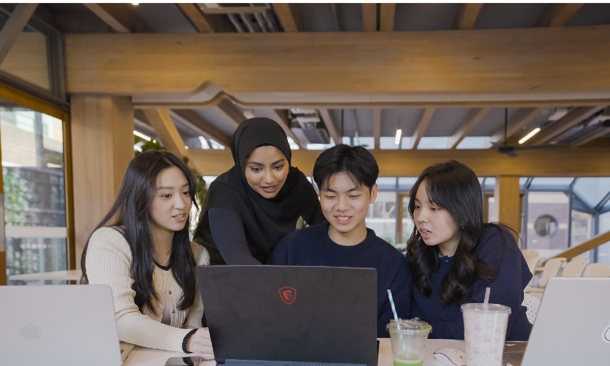 Four RMIT students sitting at a table looking at a laptop