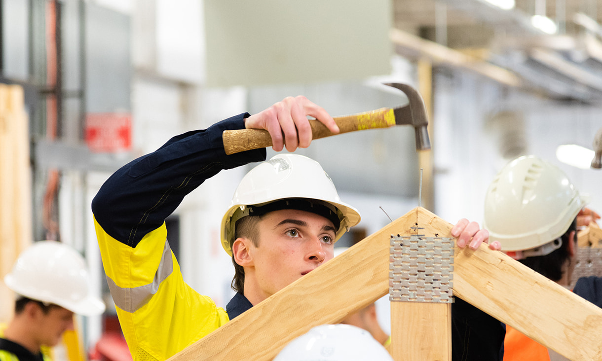 male student holding hammer while looking at wood frame