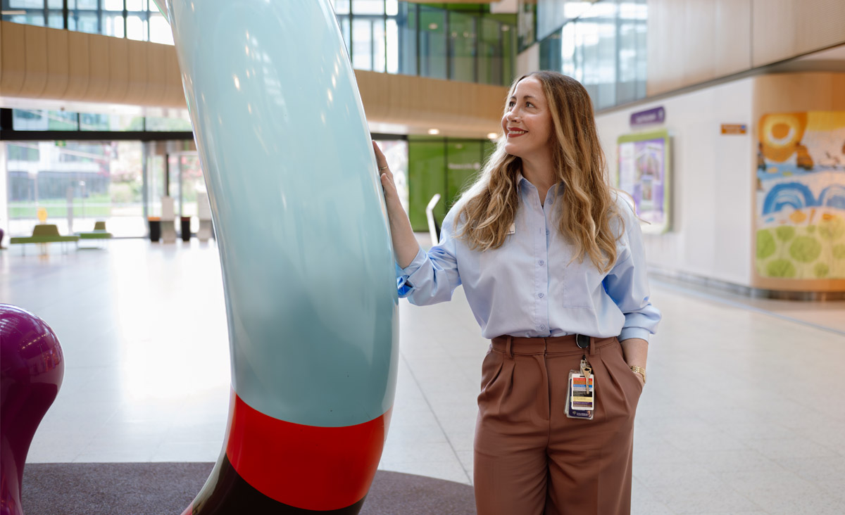 RMIT alumni Carmen Barry standing in the foyer of a hospital leaning against a sculpture