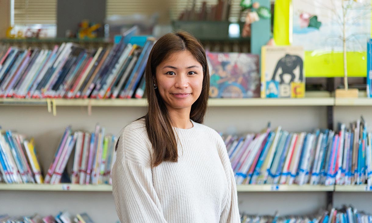Image of female student in white shirt in front of library shelves.