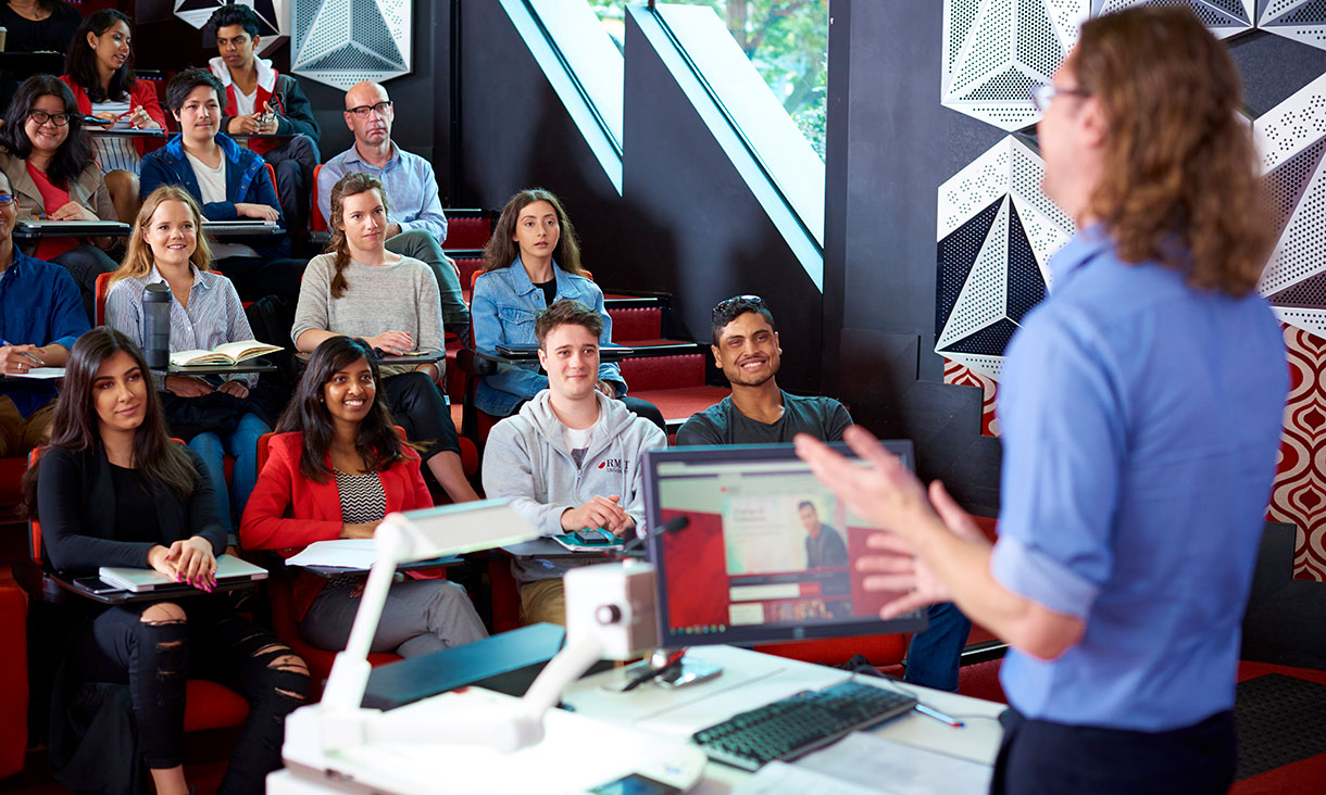 Lecturer stands in front of class in lecture room
