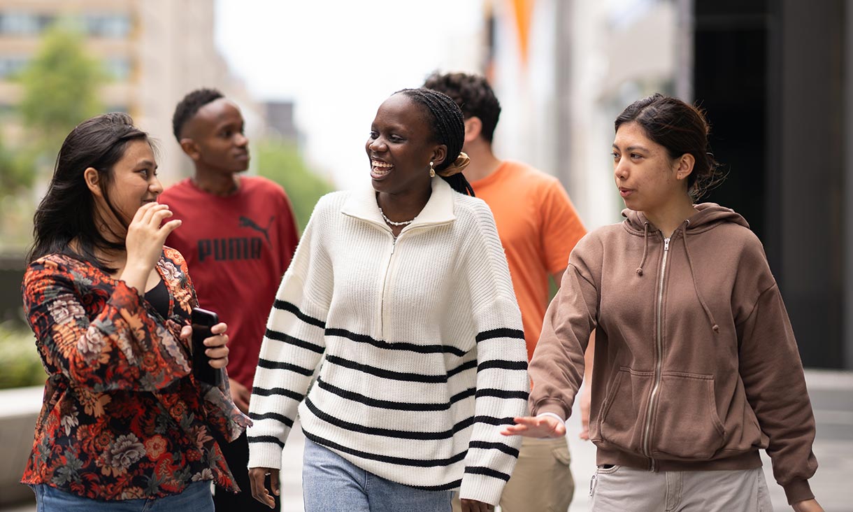 Group of five students in conversation walking outside.