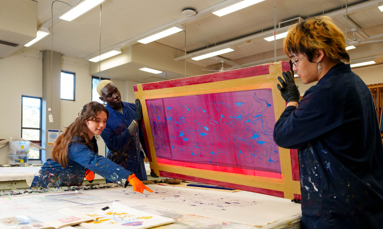 Three RMIT fashion students pressing ink patterns onto a piece of fabric