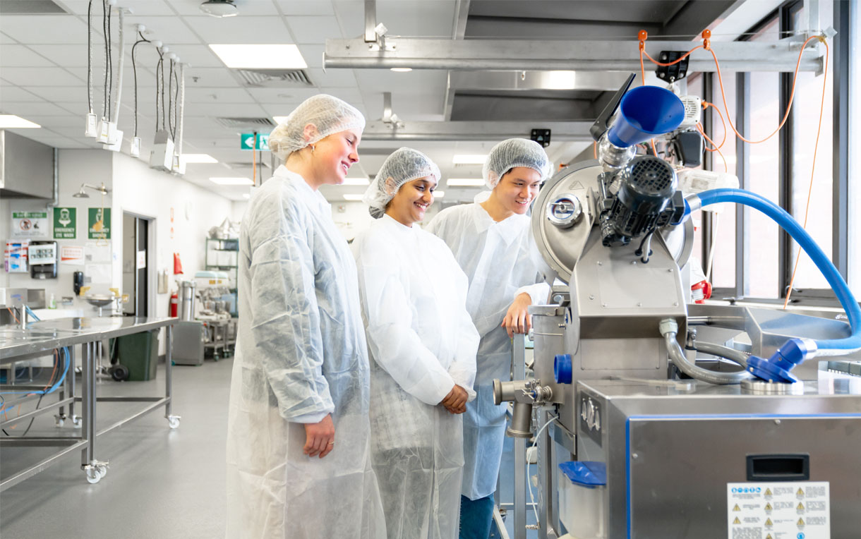 Three students looking at industrial food processing equipment on the RMIT Bundoora campus