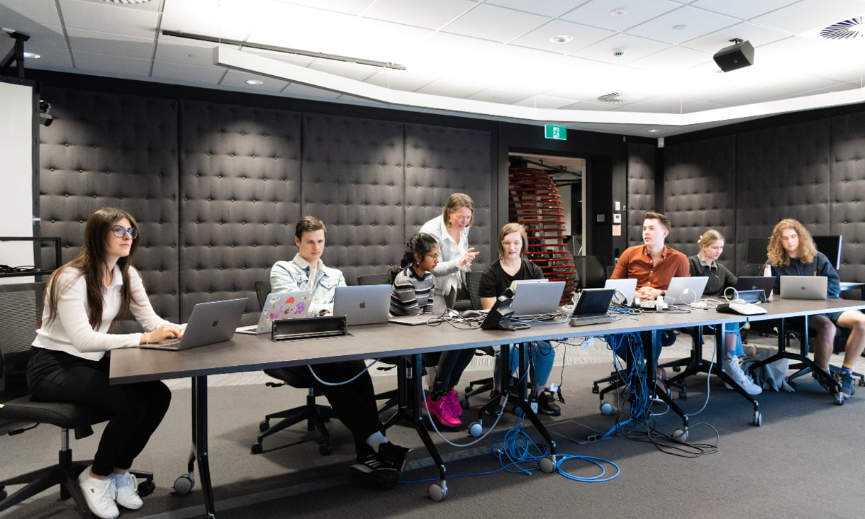 Seven students working on laptops in a high-tech lab