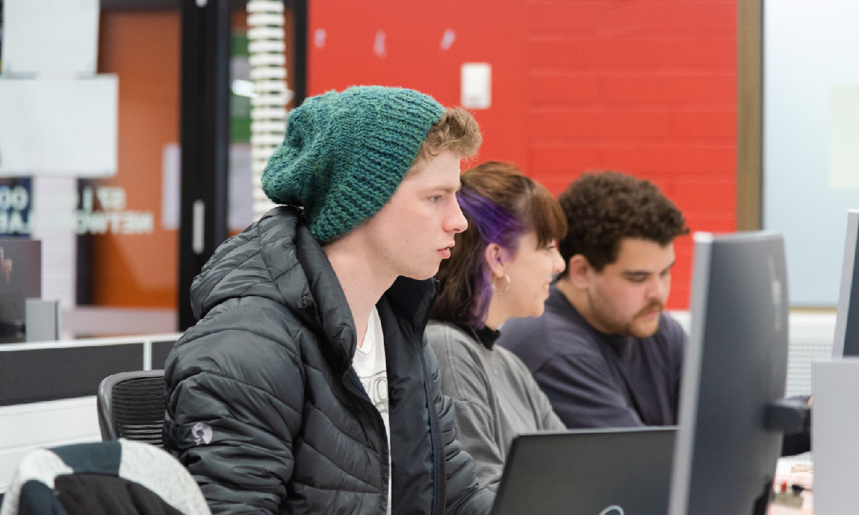 Three students sitting in a lab working on desktop computers