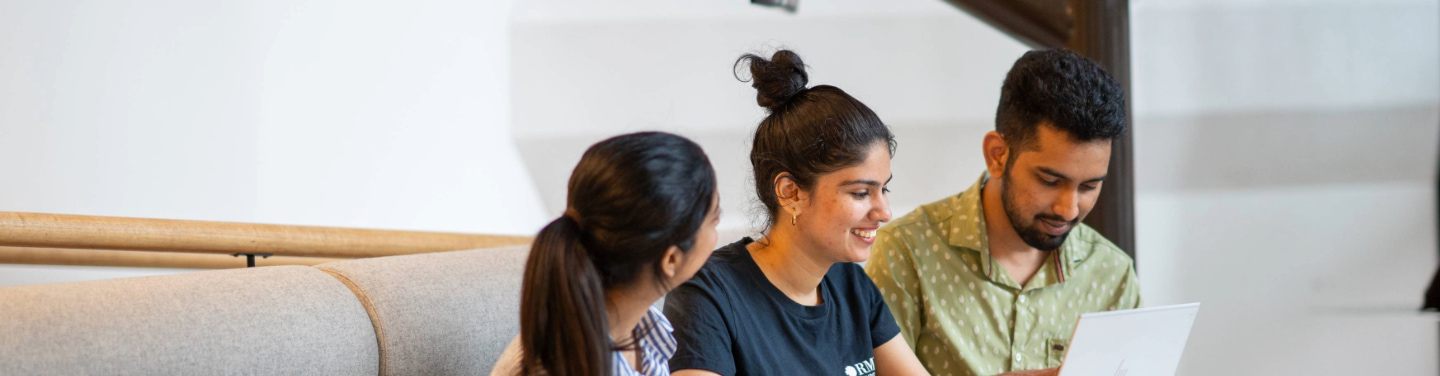 Three students walking and chatting outdoors on a university campus.