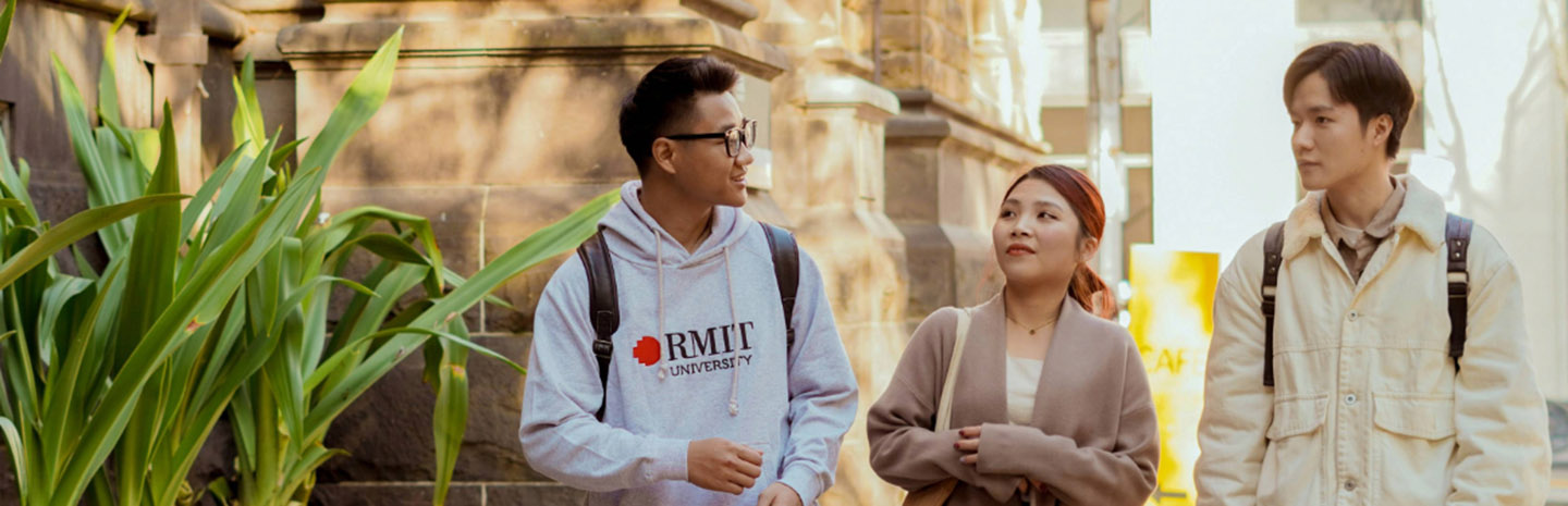 Three students walking and chatting outdoors on a university campus.