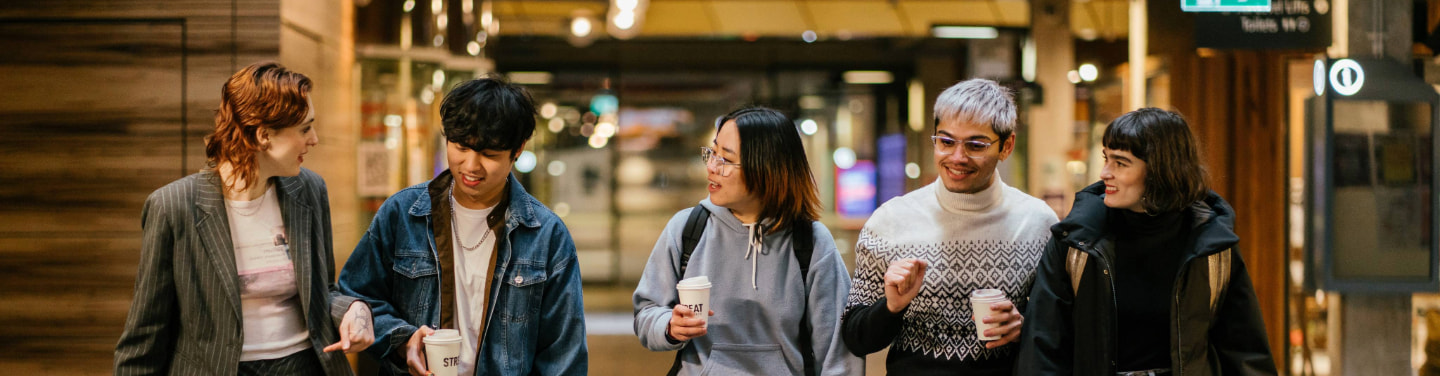 Five students walking and chatting outdoors on a university campus