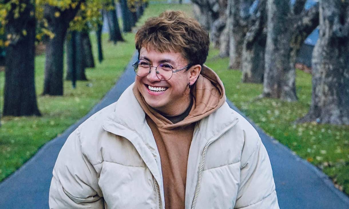 Male student outside in park with light coloured puffer jacket.