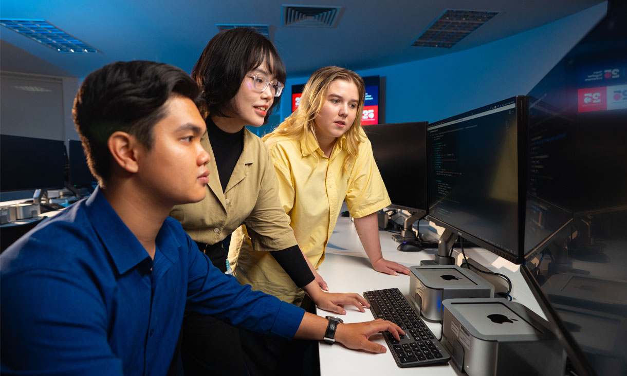 Three students working on a computer in a lab