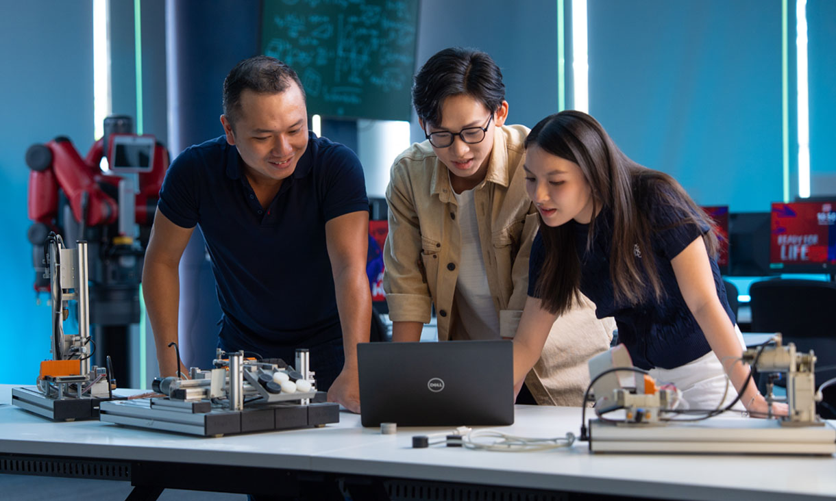 Three RMIT IT students in a computer and robotics lab working on a project together