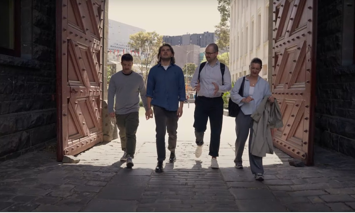 4 postgraduate students walk through two large doors at the RMIT city campus.