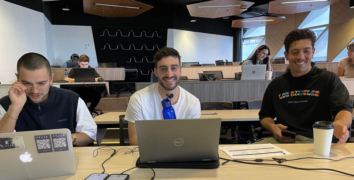 James, Oscar & Luke sitting in front of a large desk, looking at laptops while talking on a podcast.