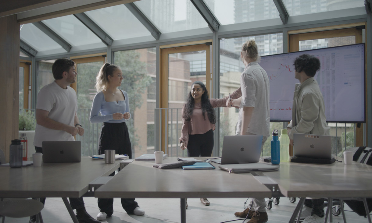 Vinisha pointing to large screen with data graph, while 4 students look towards the screen