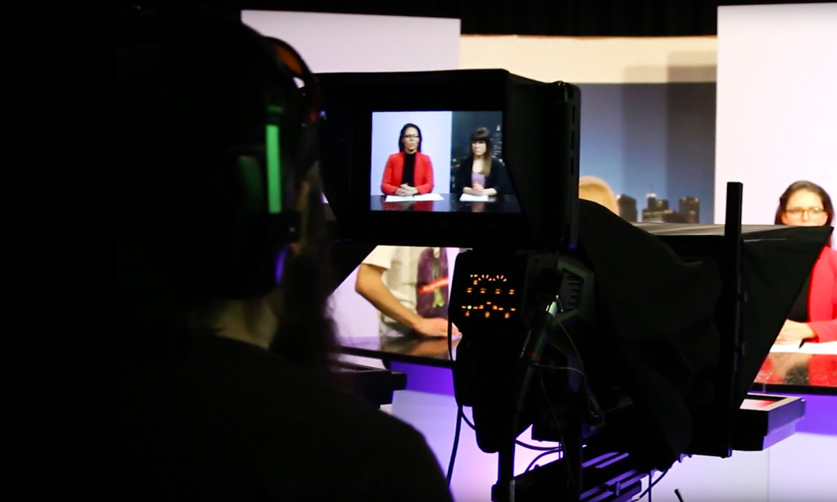Student looking trhough camera viewfinder while filming panel 