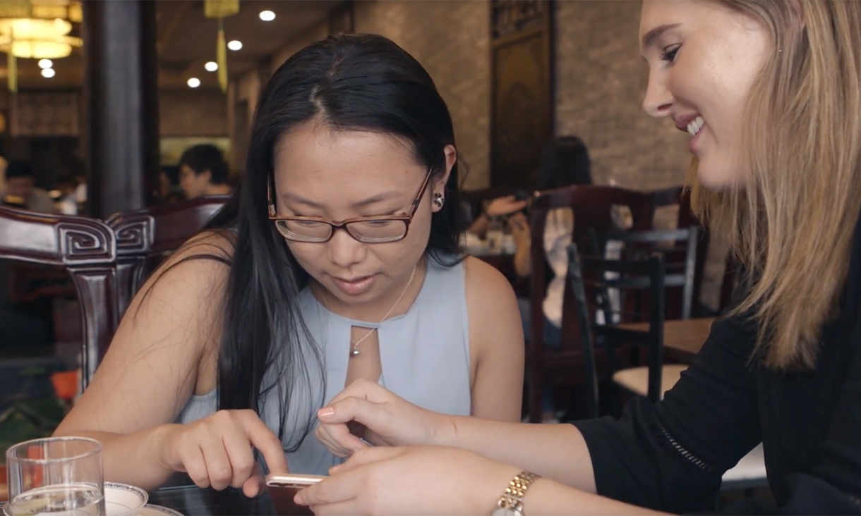 Alice Slevison, RMIT International Studies student, talking to a female, inside a cafe, both looking at a phone