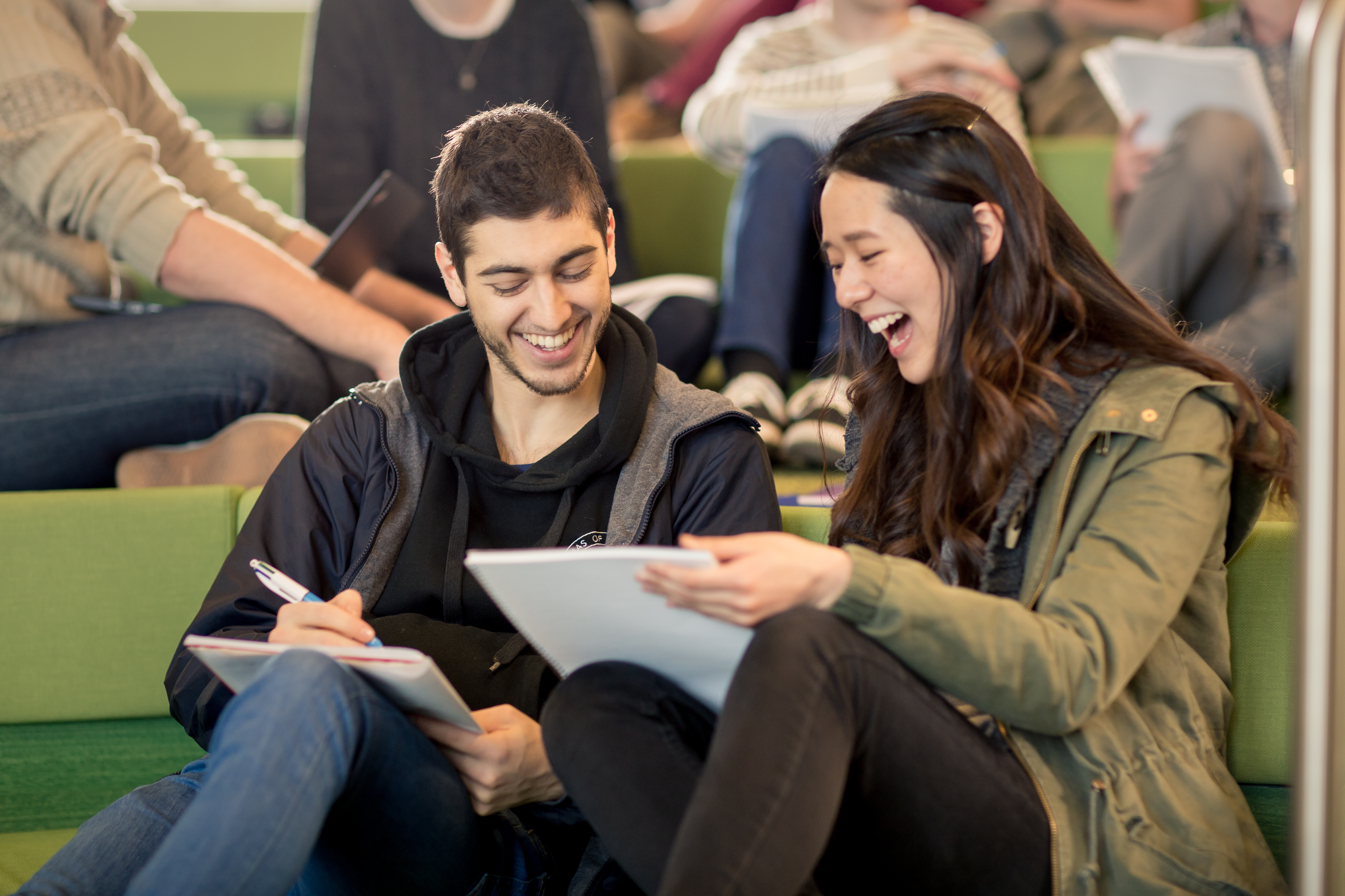 Two students smiling, casually seated and sharing work