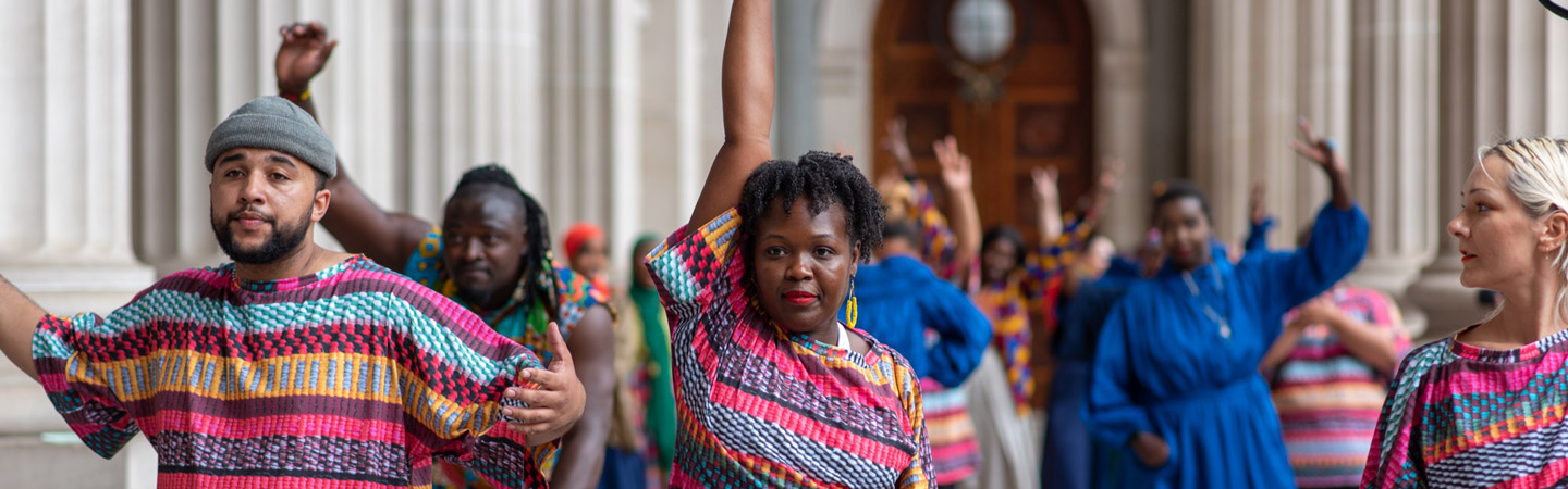 A group of people in colourful clothing, each with a fist and arm raised in the air. Cropped. 