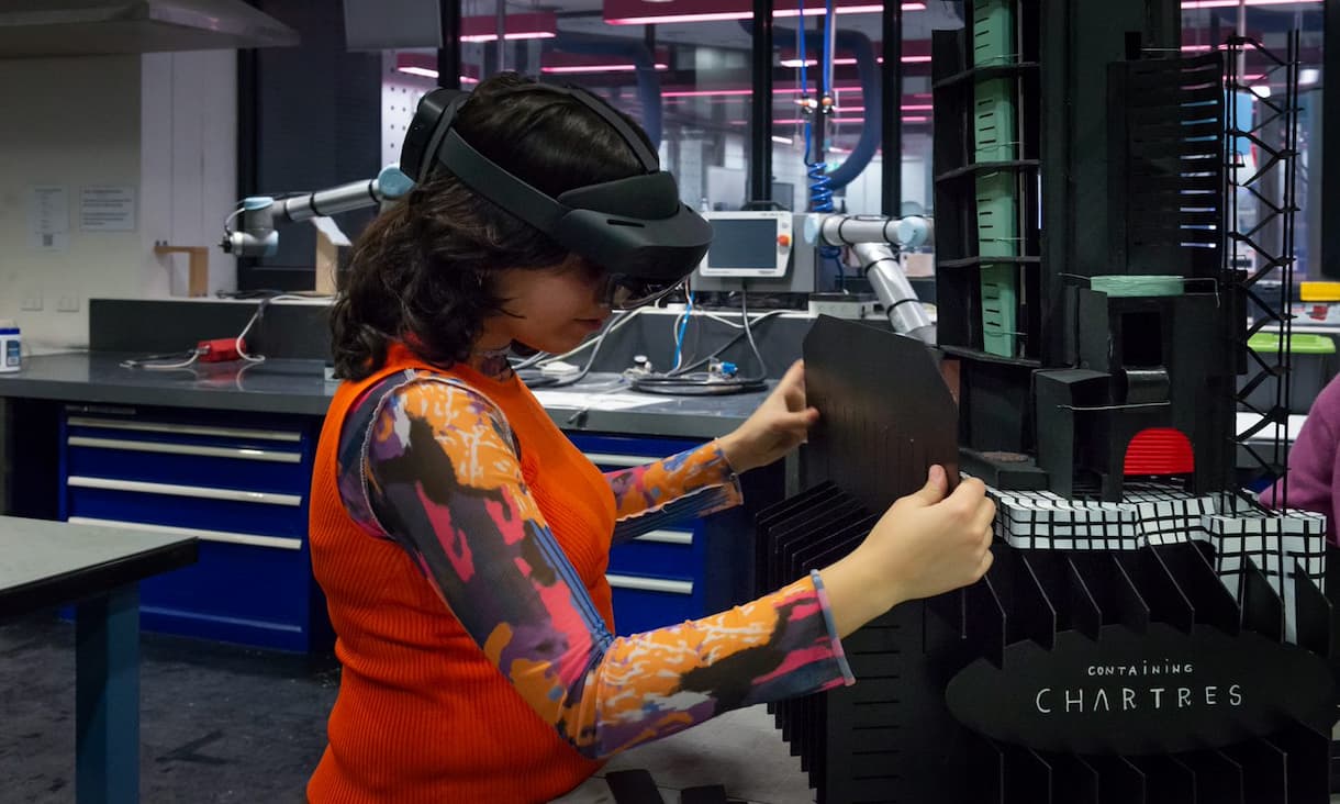 Student in an orange top wears an orange top and a VR headset as she builds the Greek God Dad Bod Pavilion.