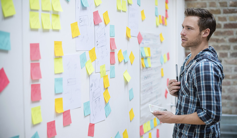 Male student standing in front of white board with many coloured "post-it" notes stuck all over it