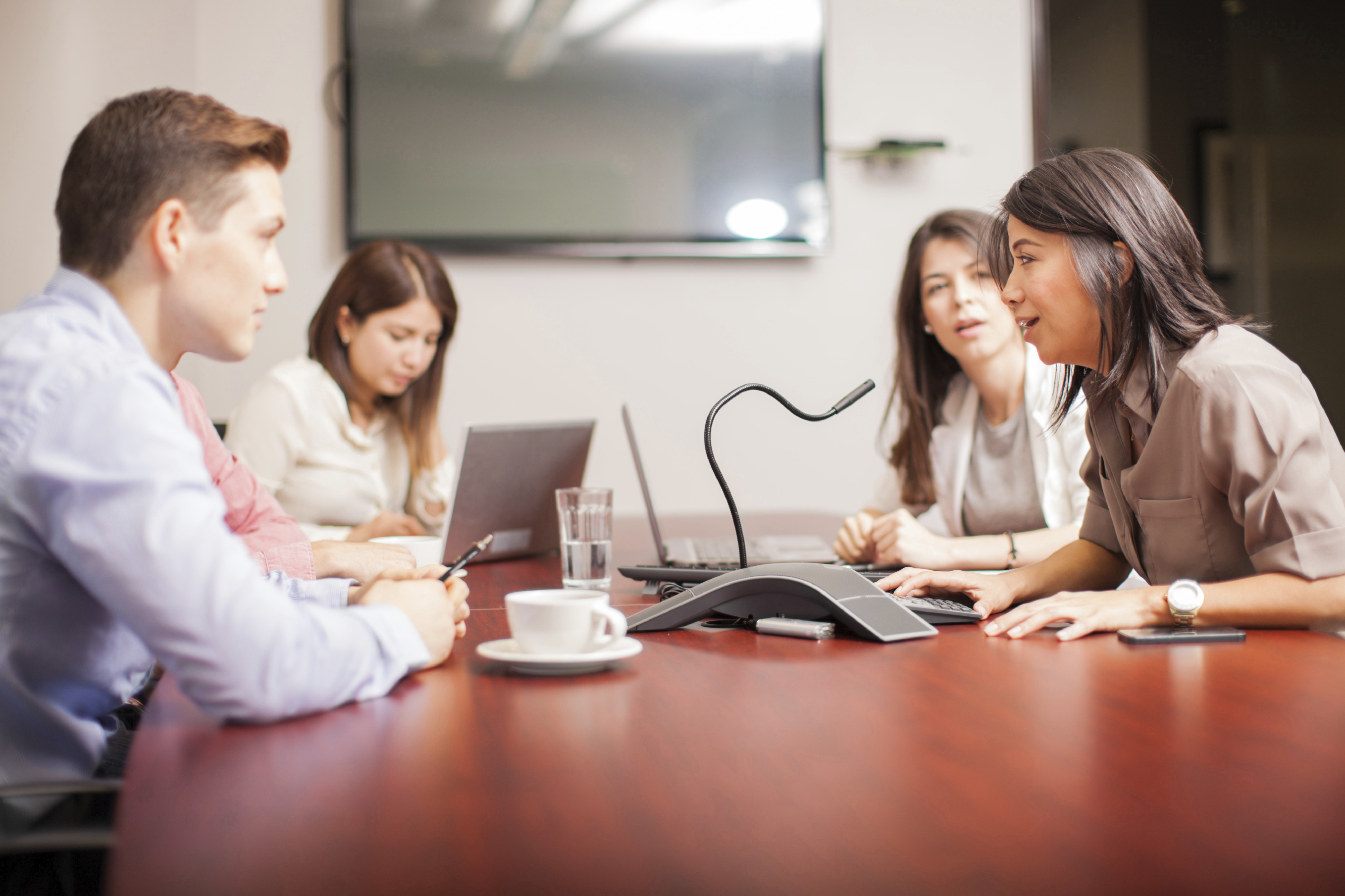 Employees sitting at large corporate desk, talking into a microphone/telephone device