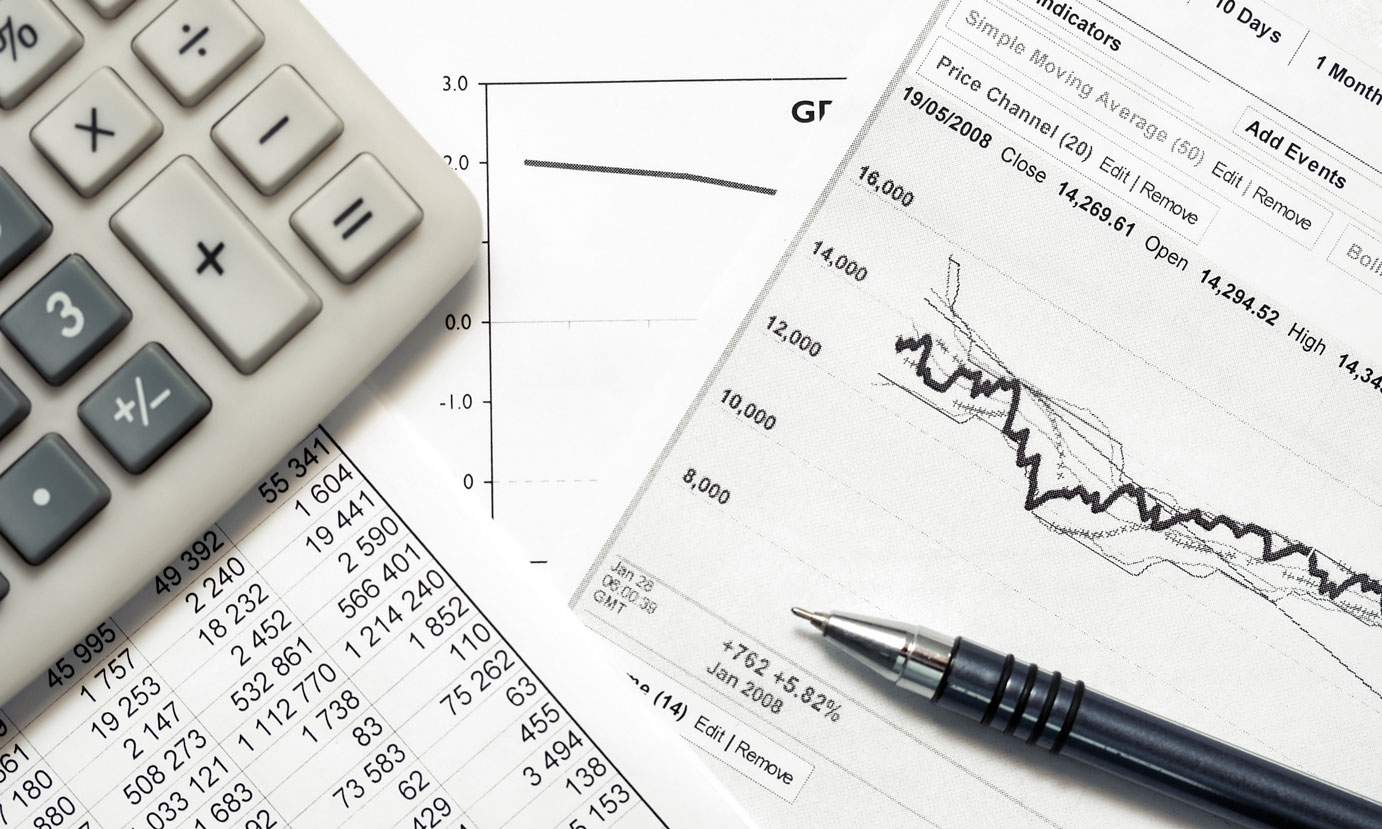 Close up shot of calculator, pen, and printed pages containing tables of data and graphs 