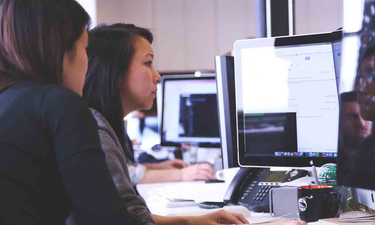 Two female business information technology students looking at information systems reports on a large computer screen in a business setting