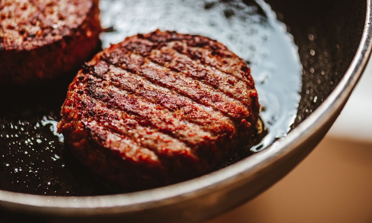 A plant-based burger patty grilling in a pan.